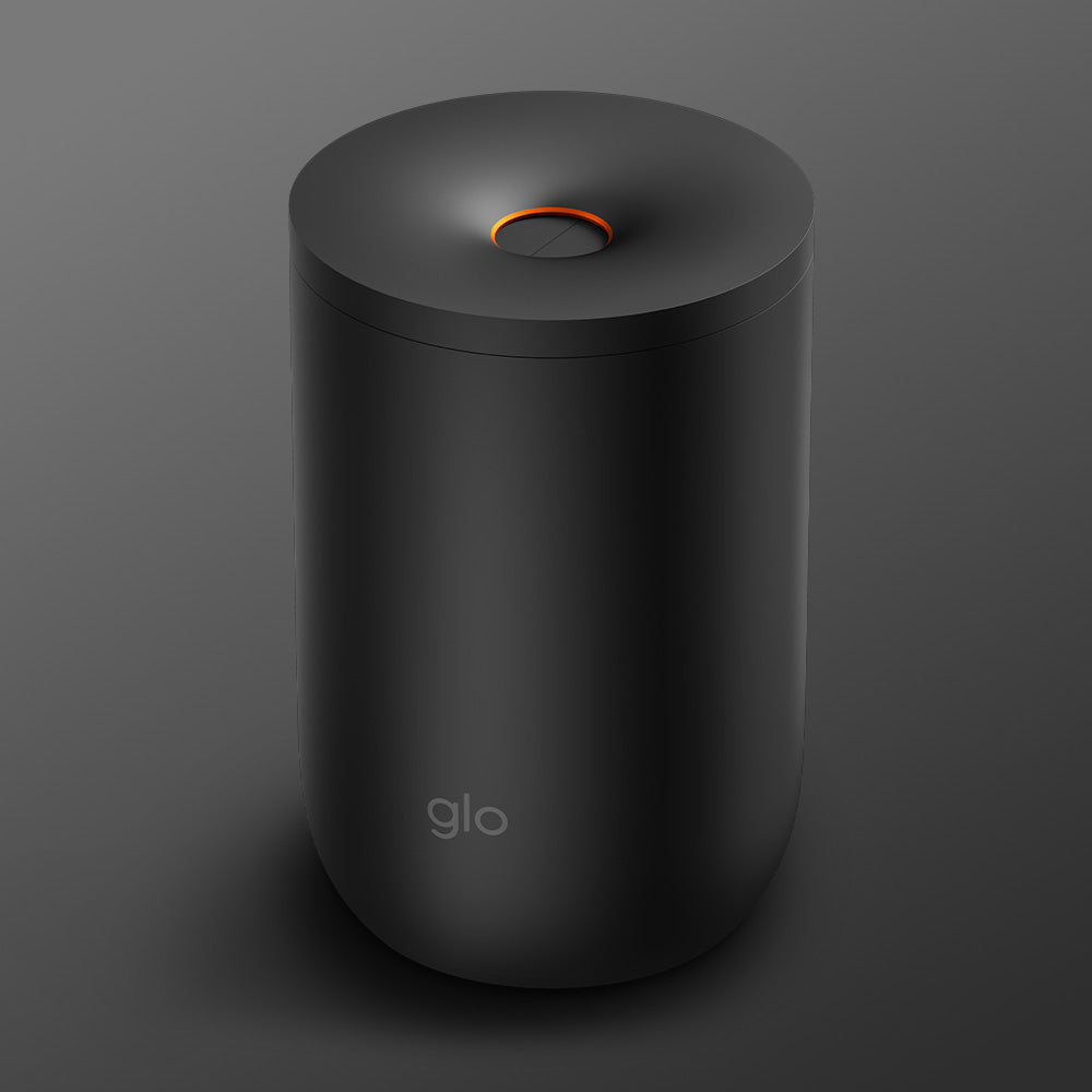 The glo™ Stick Bin is a sleek, cylindrical matte black device with a subtle glo logo near the bottom, a circular orange accent on top, and comes with a premium fabric cover for extra protection, shown against a gray background.