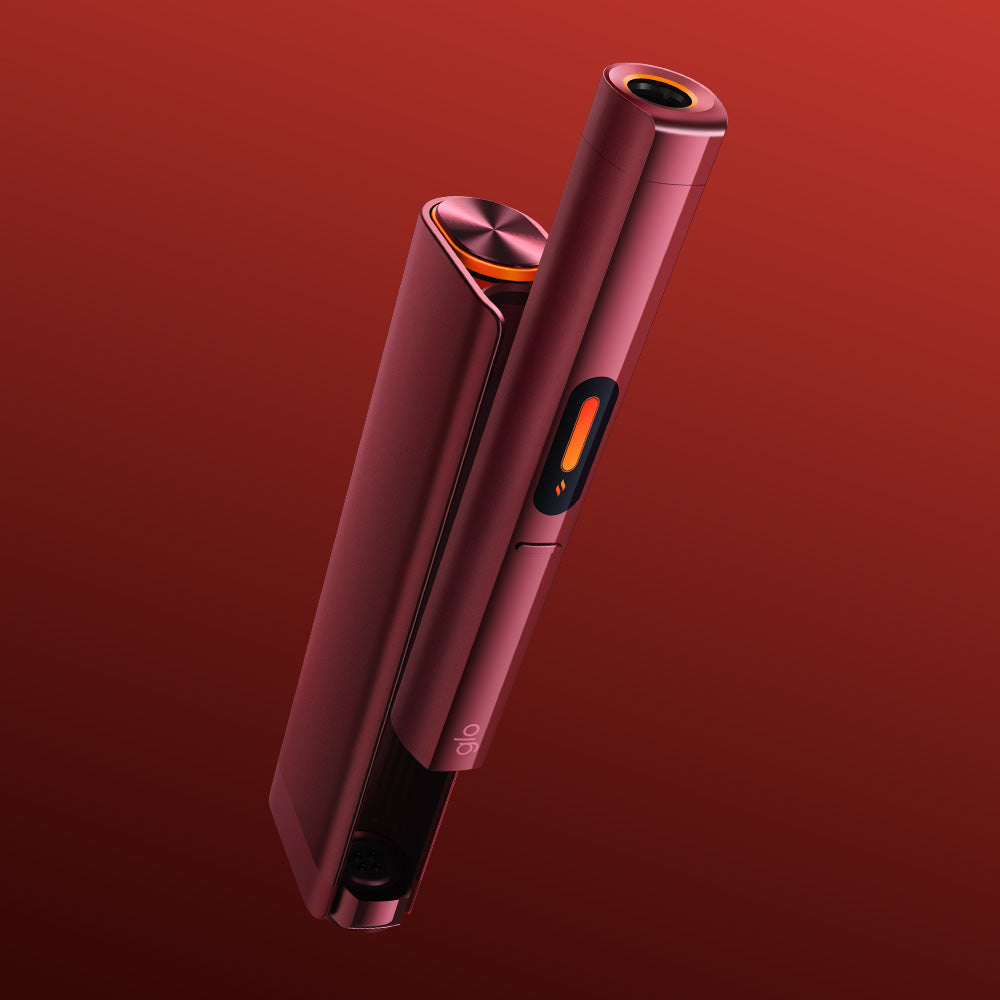 A sleek, modern red glo™ HILO Plus Charging Dock with a cylindrical shape stands upright against a gradient red background. It features a small display, circular button, and shiny metallic cap—perfect for charging or storing spare pens.