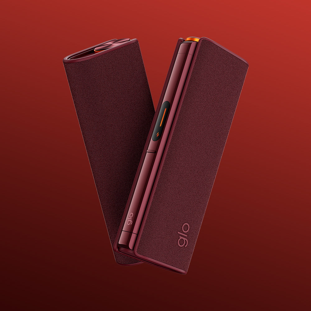 Two sleek, maroon-colored glo™ HILO devices with textured surfaces stand angled on a red gradient background. Both display the "glo" branding near the base and are styled with the protective glo™ HILO Plus Sleeve for added flair.