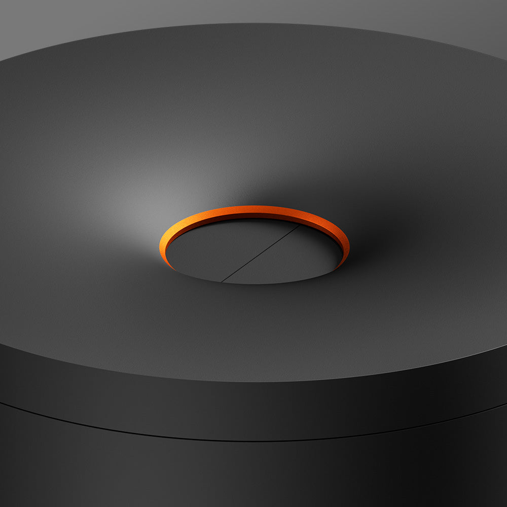 The glo™ Stick Bin features a sleek, matte black cylindrical design with a shallow concave top, a recessed orange accent at the center, and a premium fabric cover for added device protection and modern minimalism.