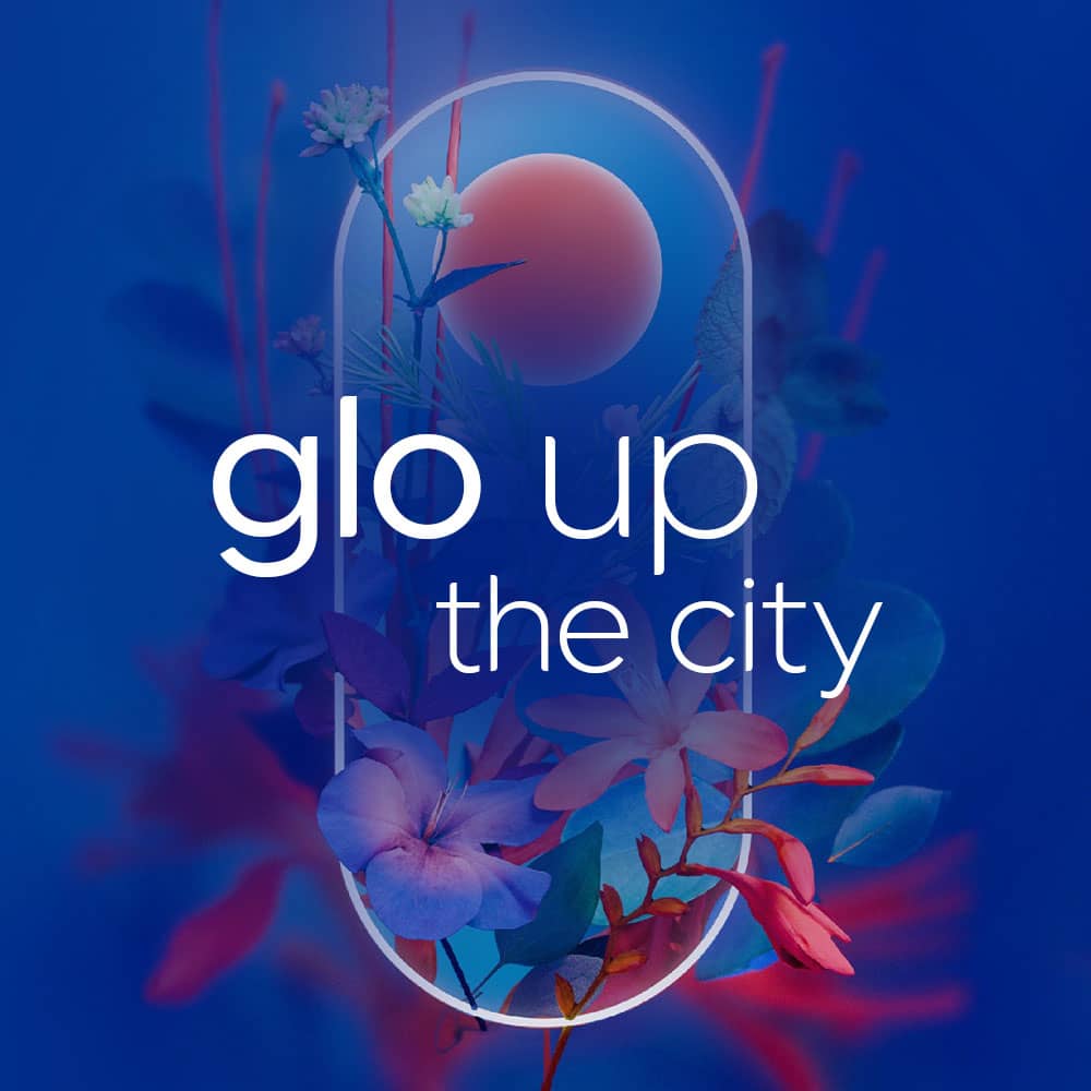 Bright floral design with a glowing oval frame, a red sun, and colorful flowers on a blue background. White text in the center reads: glo up the city.