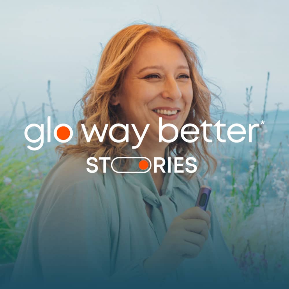 A smiling woman with wavy hair holds a small device. Overlaid text reads glo way better* STORIES with an outdoor background of plants and a blurred landscape.
