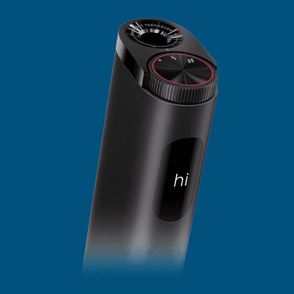 A sleek, black electronic device with a display screen showing the word hi, a red-ringed dial, and a vented top, set against a solid blue background.